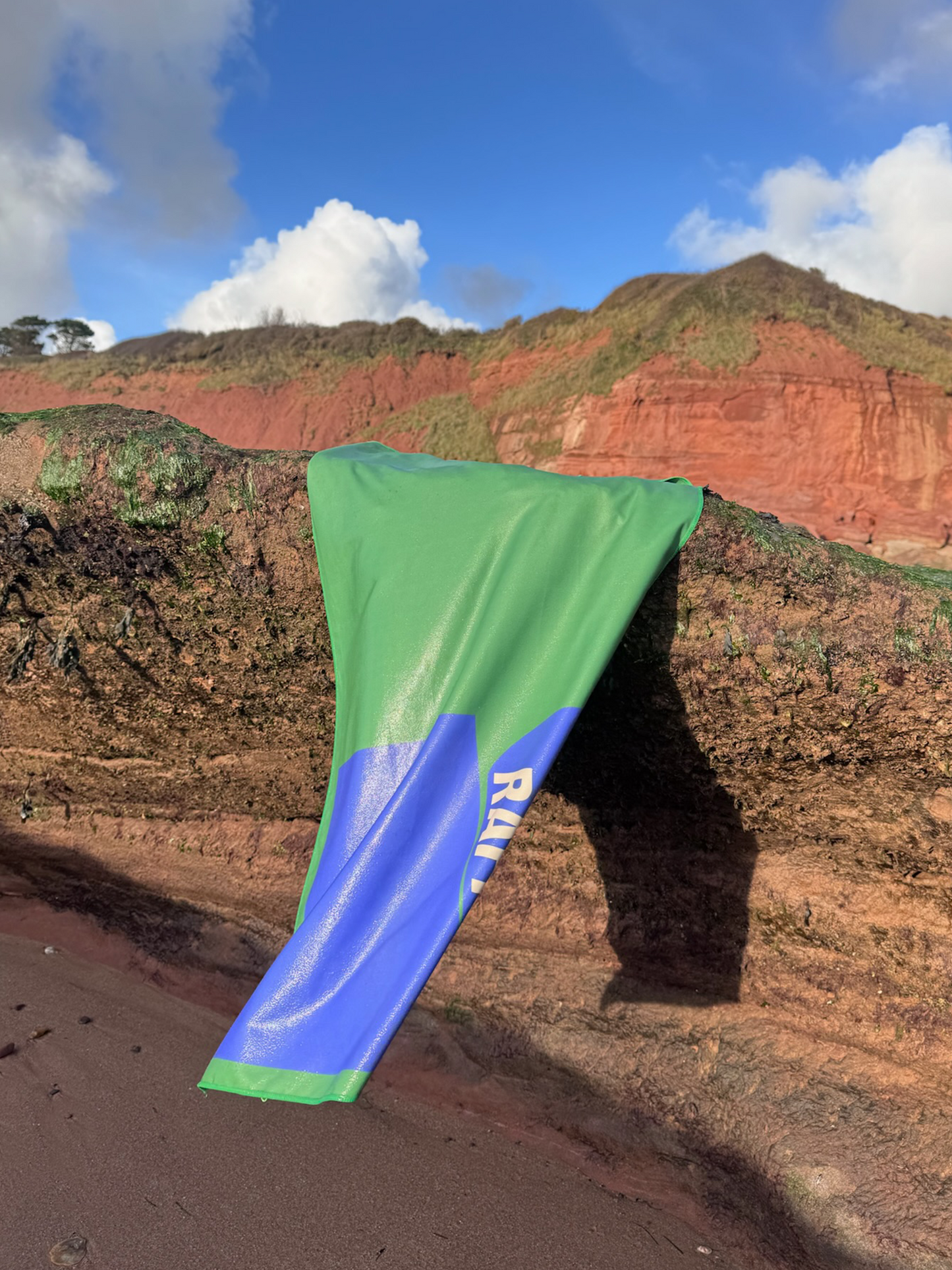 Raffilo Dog Beach Towel in Seagrass & Tide, placed on rocks, perfect for outdoor adventures and post-swim drying.